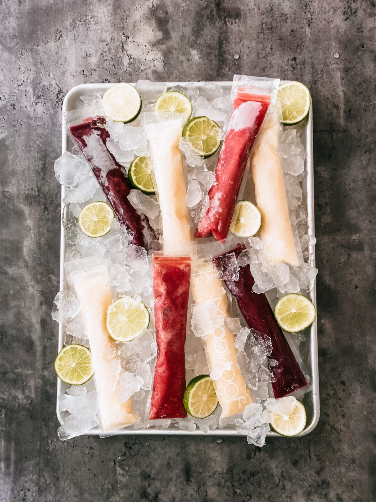 Homemade freezer pops on a tray of ice with sliced limes.