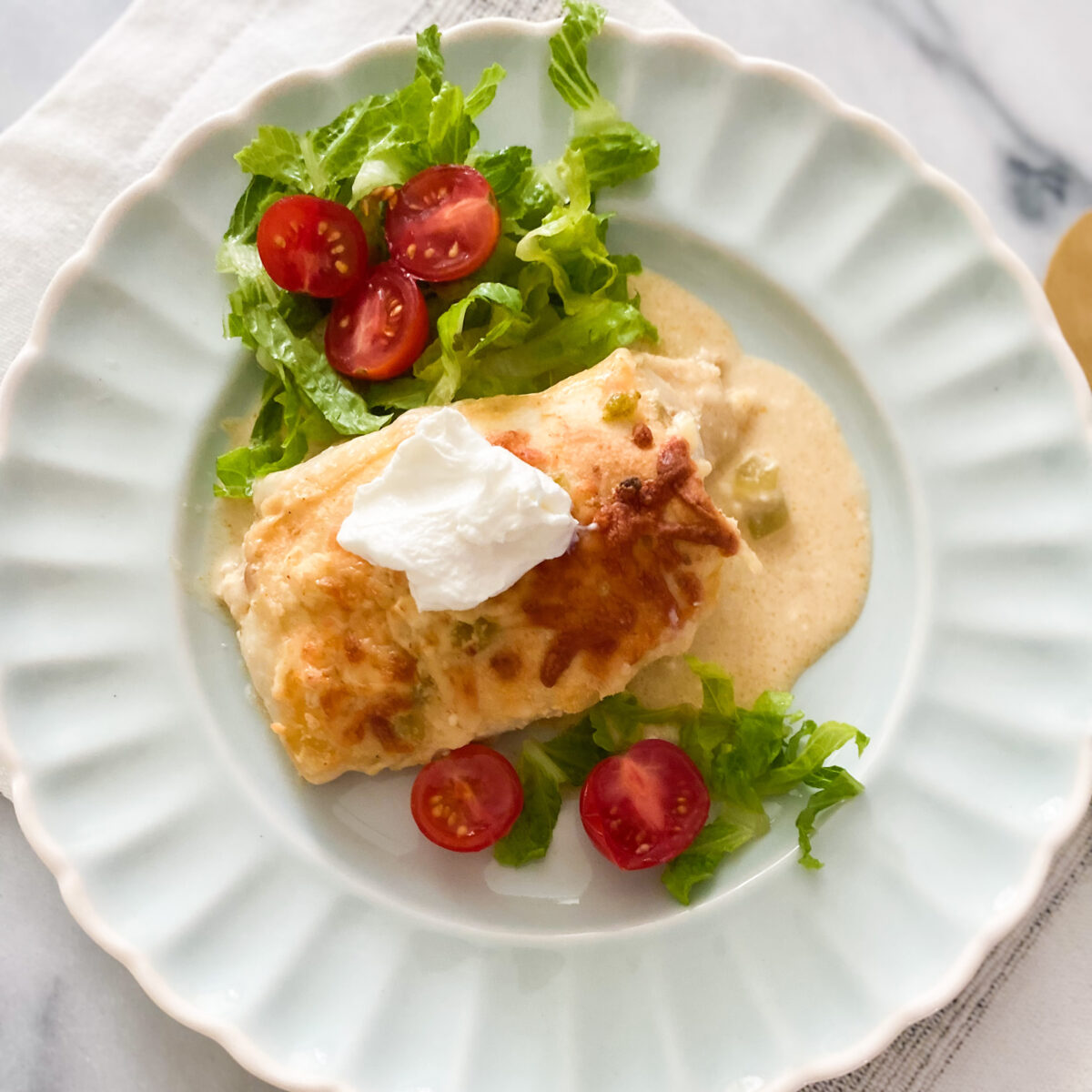 An enchilada on a plate with side salad and sour cream on top.