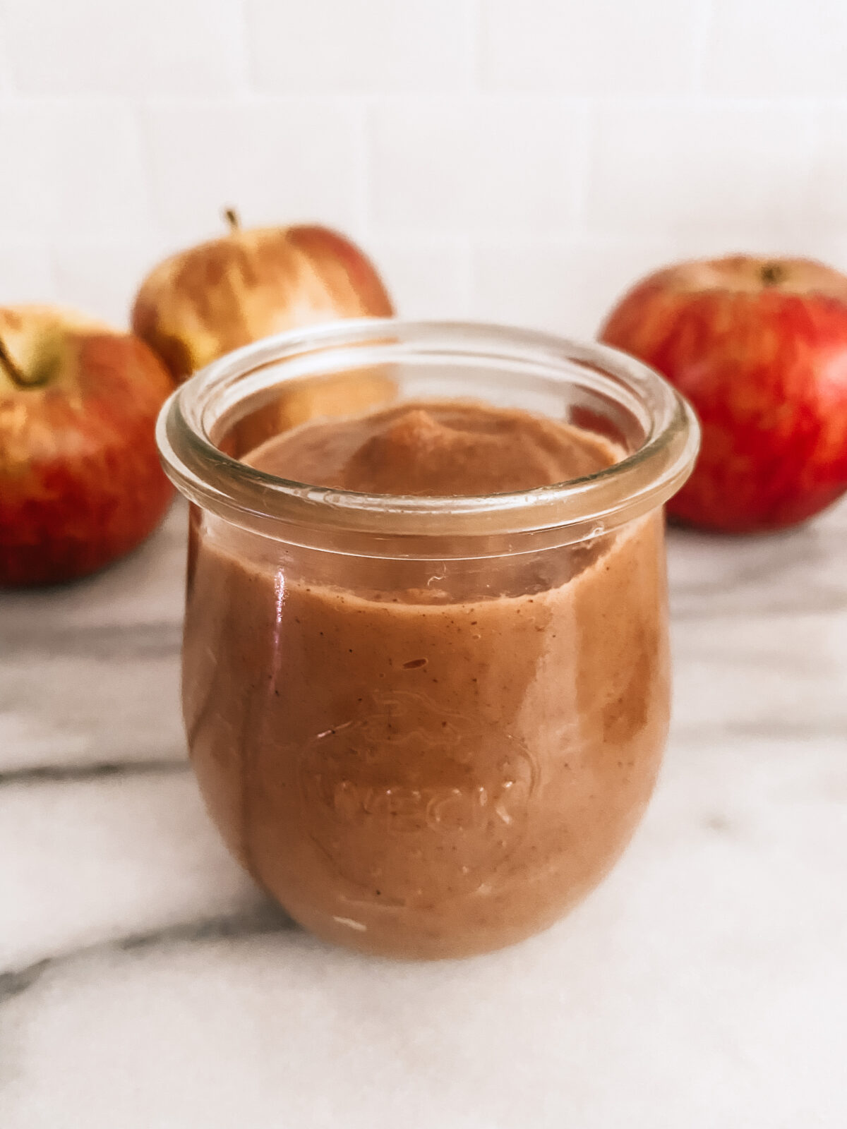 A jar of slow cooker apple butter sitting on a counter surrounded by Honeycrisp apples.
