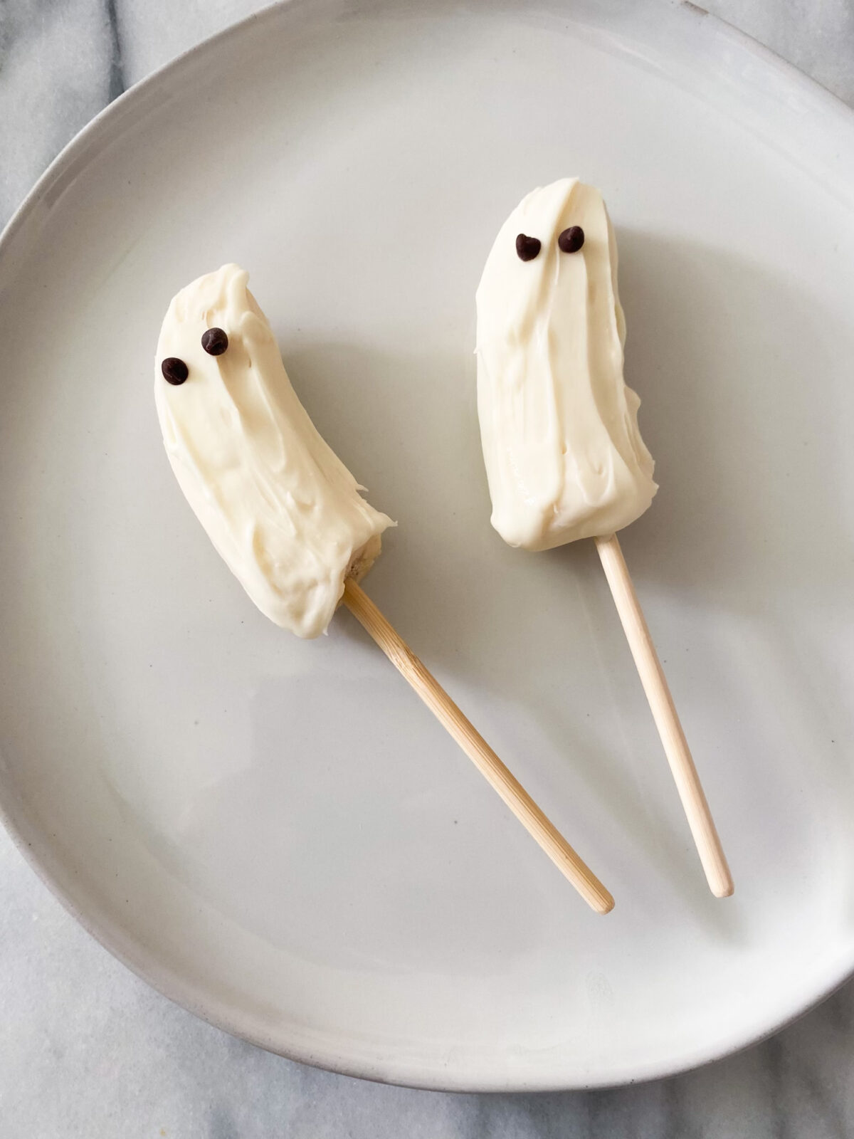 Two halves of a banana on skewers and dipped in white chocolate with mini chocolate chips as eyes. 