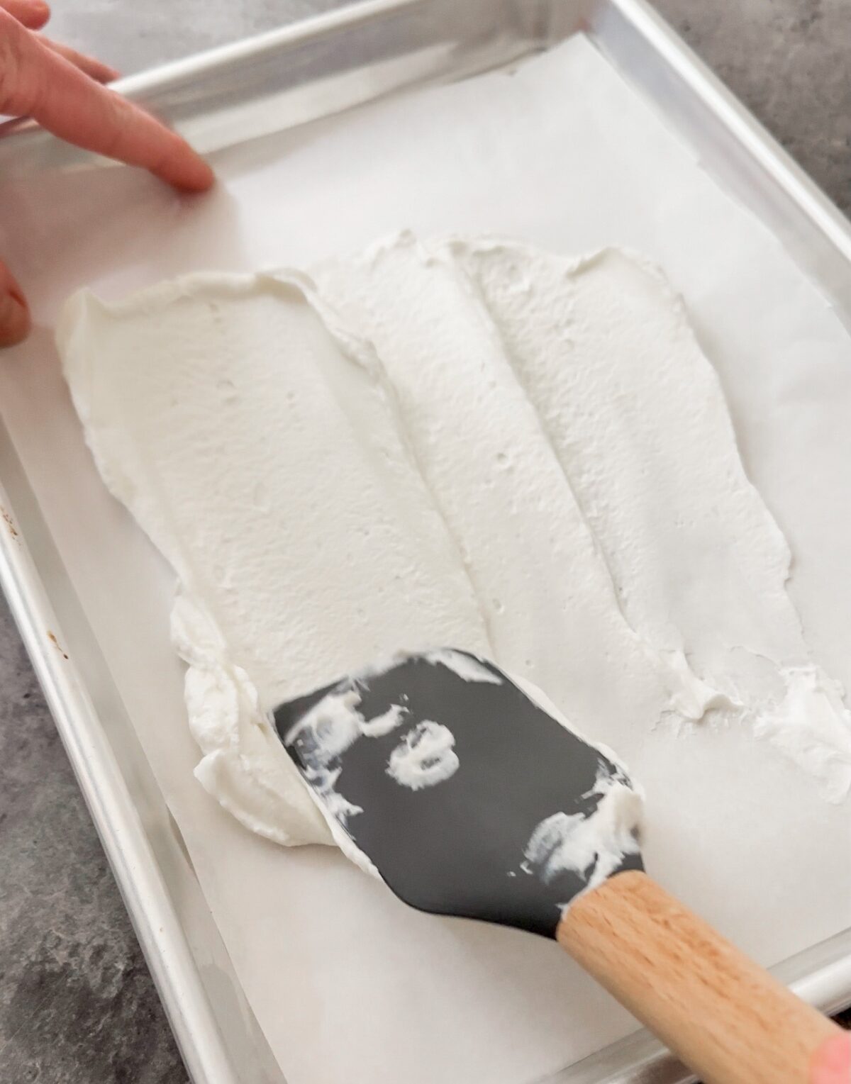 spatula spreading yogurt onto a parchment lined baking sheet
