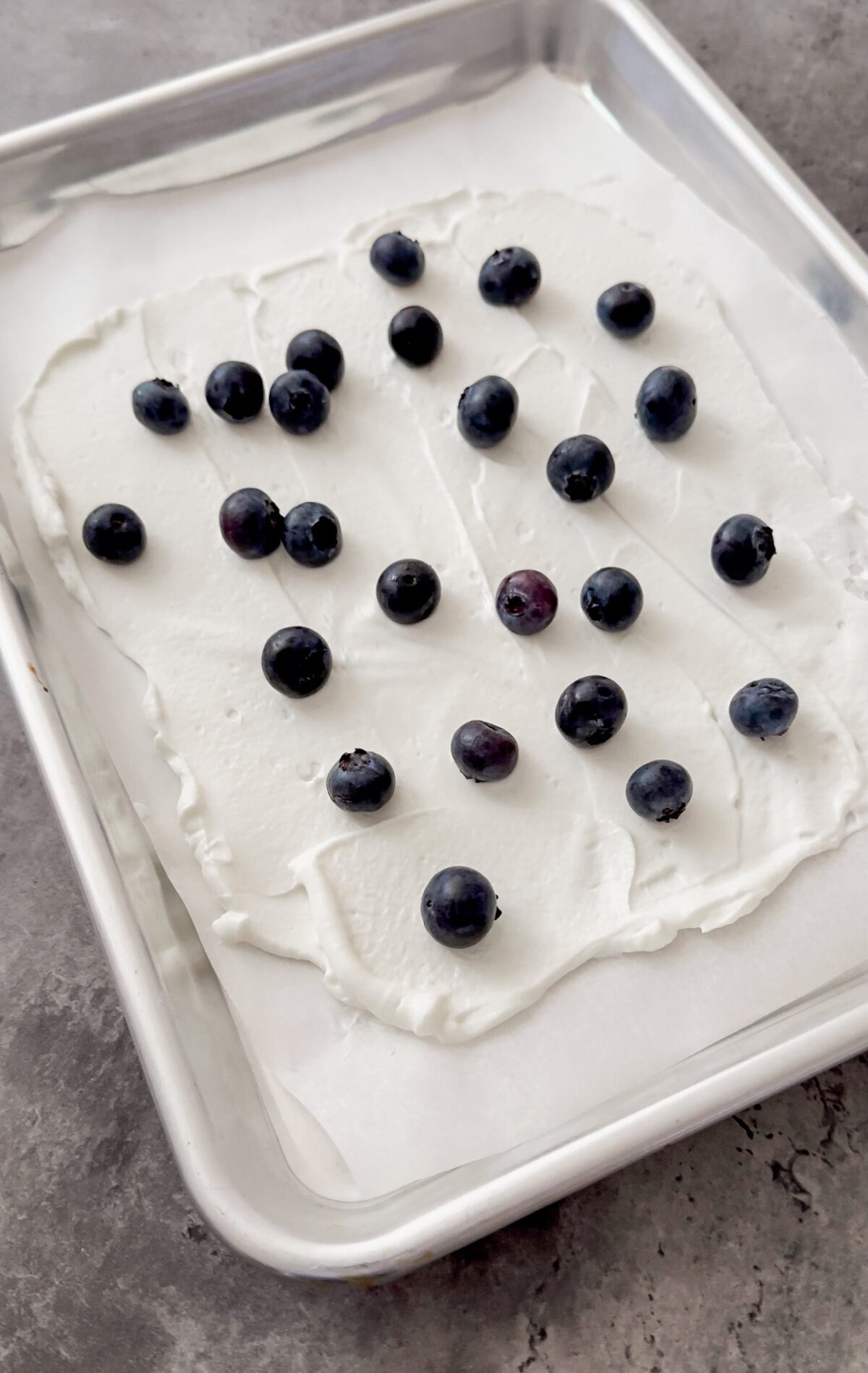 blueberries sprinkled on yogurt spread on baking sheet

