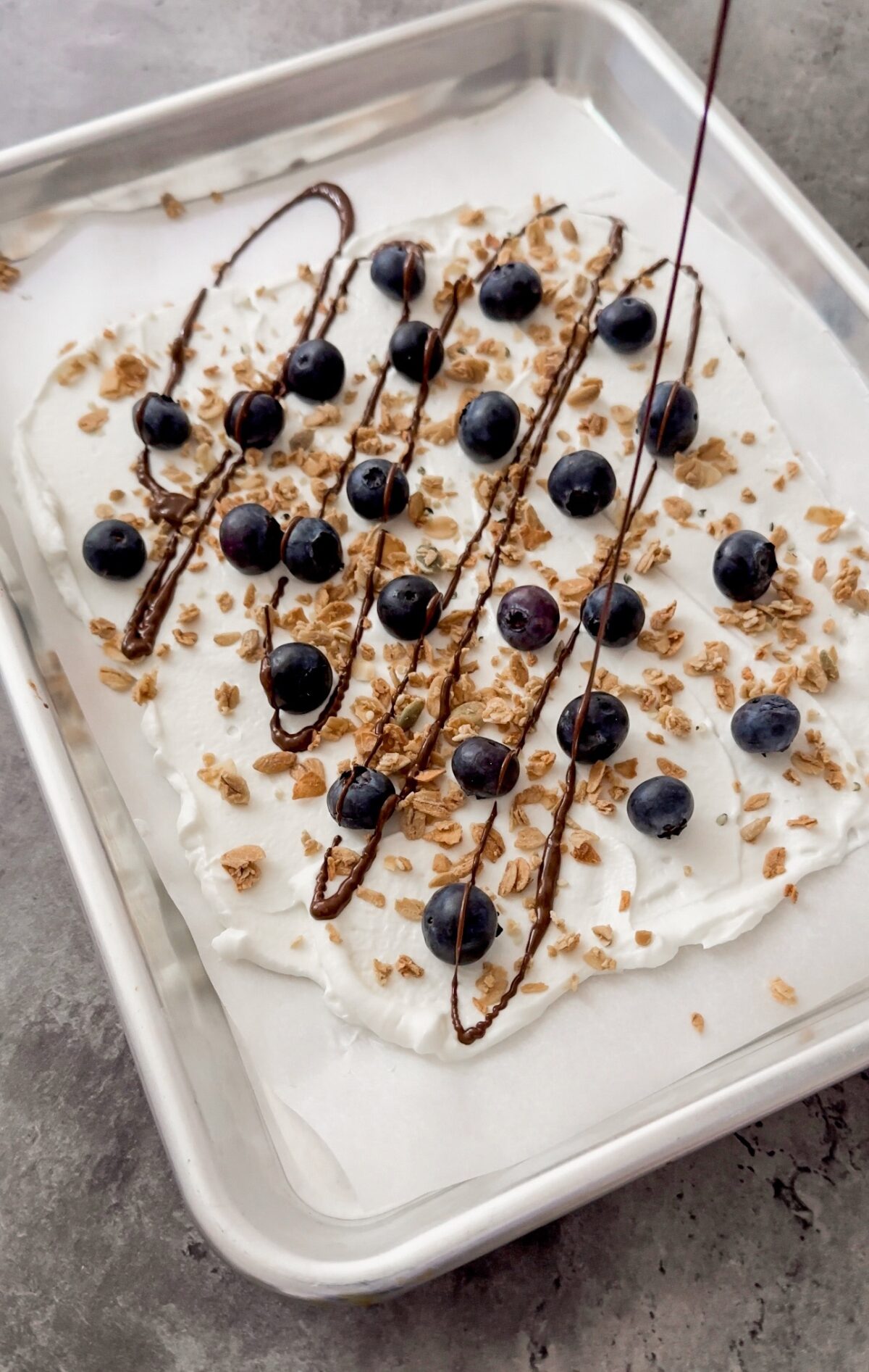 chocolate being drizzled on yogurt spread over baking sheet
