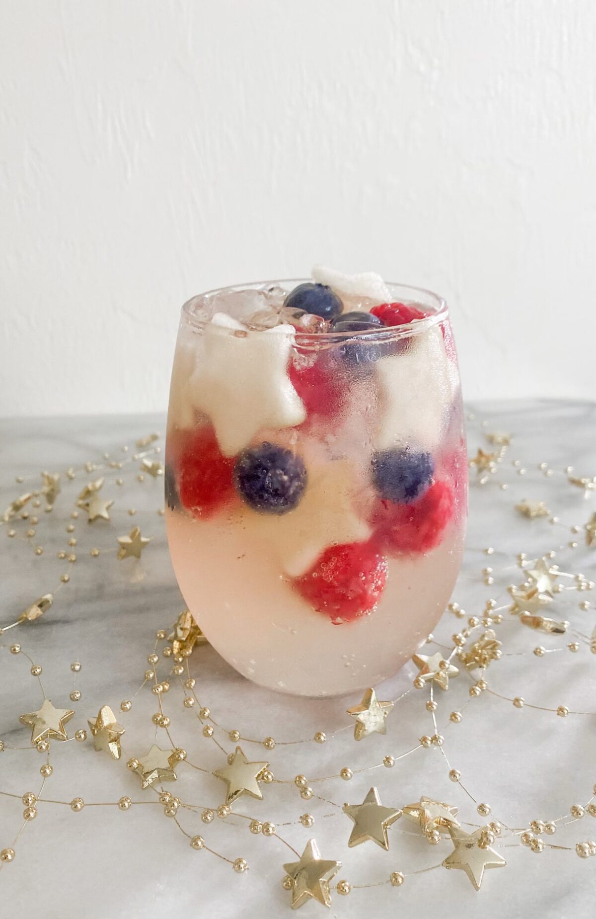 a glass of sparkling sangria garnished with apple stars, raspberries and blueberries
