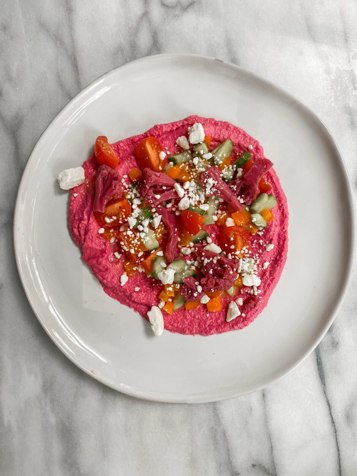 a plate of beet hummus topped with pickled and fresh vegetables and feta crumbles