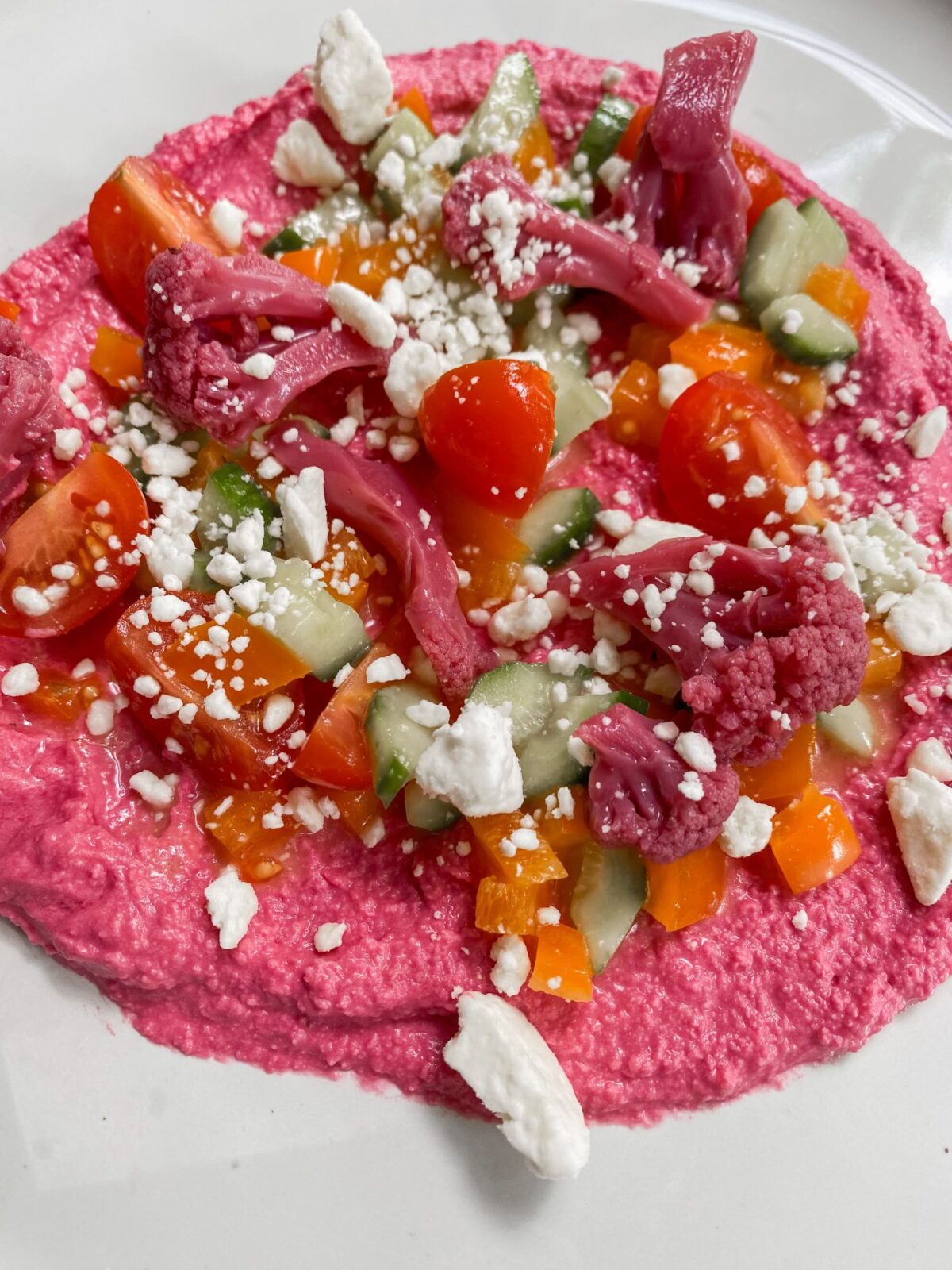 plate of beet hummus topped with fresh veggies and feta cheese
