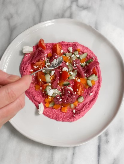 beet hummus with vegetables and feta cheese being sprinkled on top

